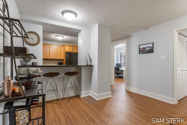 kitchen with dark countertops, baseboards, wood finished floors, black refrigerator, and a kitchen breakfast bar