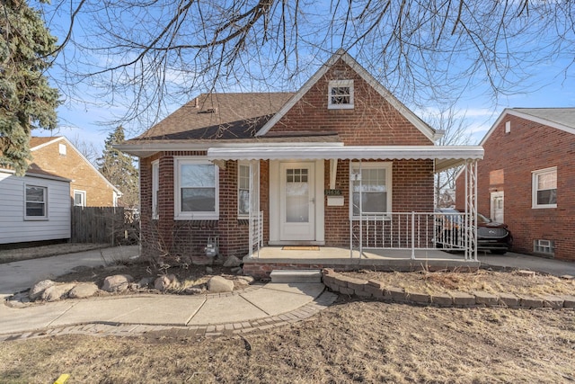 bungalow featuring brick siding, a porch, and fence