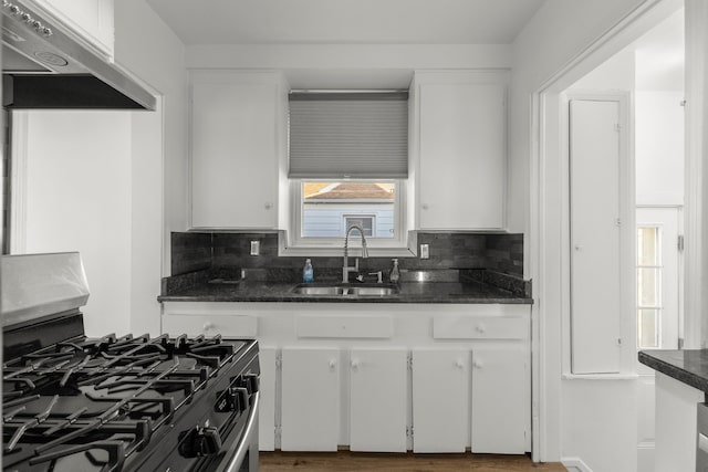 kitchen with backsplash, under cabinet range hood, gas stove, white cabinetry, and a sink