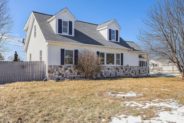 view of front of home featuring a front yard, fence, stone siding, and a shingled roof