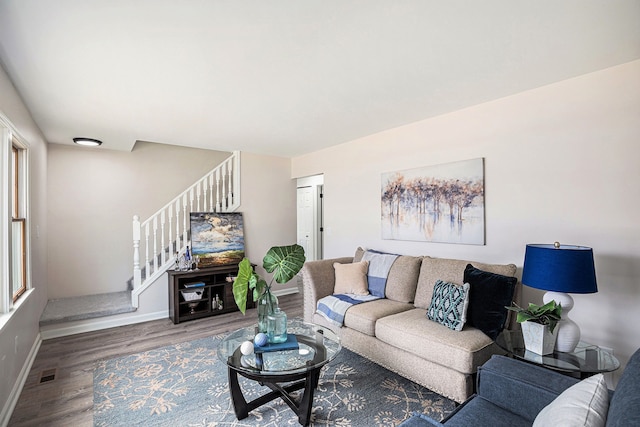 living room featuring stairway, baseboards, visible vents, and wood finished floors