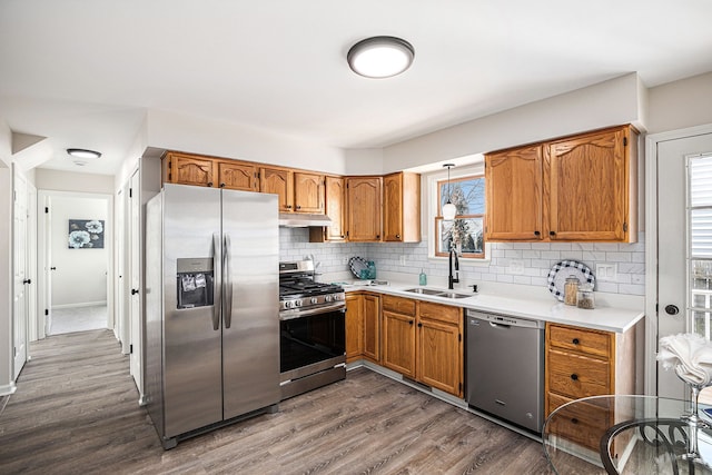 kitchen with dark wood-style floors, a sink, stainless steel appliances, under cabinet range hood, and backsplash