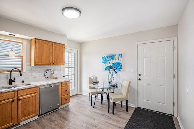 kitchen featuring dishwasher, light countertops, decorative backsplash, light wood-style floors, and a sink