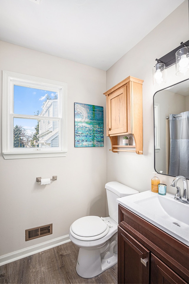 bathroom featuring visible vents, baseboards, toilet, wood finished floors, and vanity