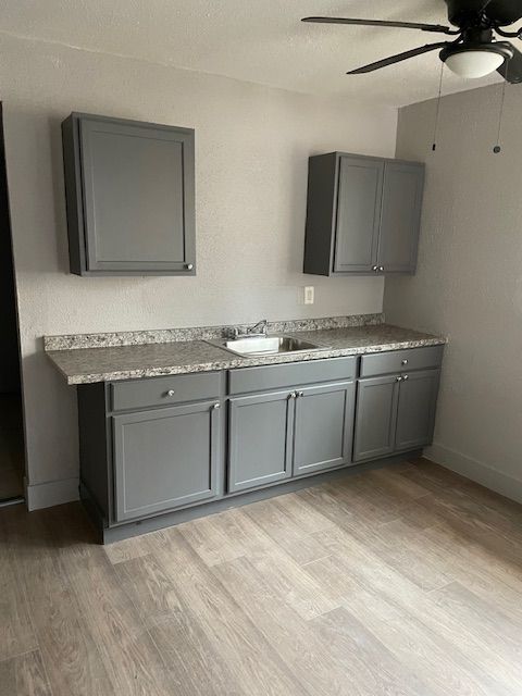 kitchen featuring light wood-style floors, a ceiling fan, gray cabinets, and a sink