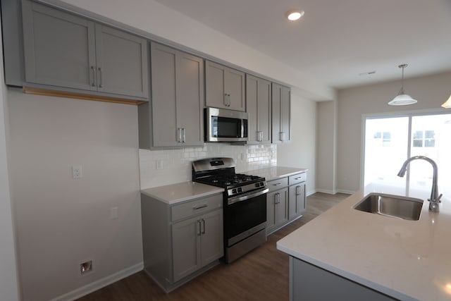 kitchen featuring dark wood-style flooring, tasteful backsplash, gray cabinetry, appliances with stainless steel finishes, and a sink