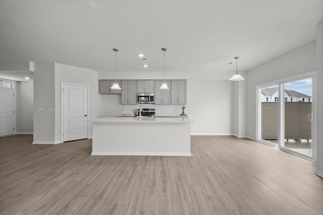 kitchen with light wood finished floors, light countertops, gray cabinets, stainless steel microwave, and baseboards