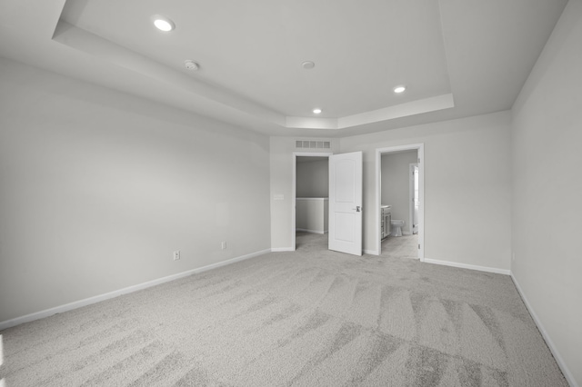 unfurnished bedroom with light carpet, a tray ceiling, visible vents, baseboards, and recessed lighting