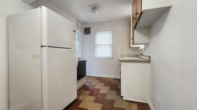 kitchen with dark floors, range with electric stovetop, visible vents, freestanding refrigerator, and a sink