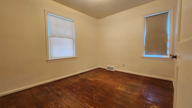 empty room with dark wood-style floors, visible vents, and baseboards