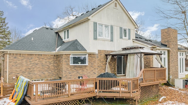 back of property featuring a gazebo, brick siding, a shingled roof, and a wooden deck