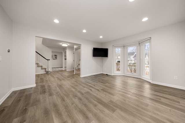 unfurnished living room featuring baseboards, stairway, wood finished floors, and recessed lighting