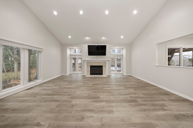 unfurnished living room with high vaulted ceiling, a fireplace, wood finished floors, and a wealth of natural light