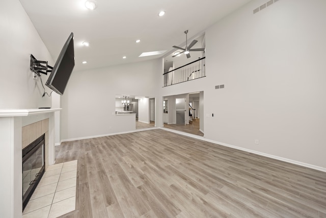 unfurnished living room with high vaulted ceiling, a tile fireplace, recessed lighting, a ceiling fan, and light wood-type flooring