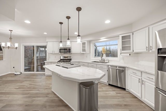 kitchen featuring stainless steel appliances, white cabinets, a sink, a kitchen island, and light wood-type flooring