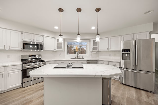 kitchen with light stone counters, stainless steel appliances, a sink, white cabinetry, and light wood-type flooring