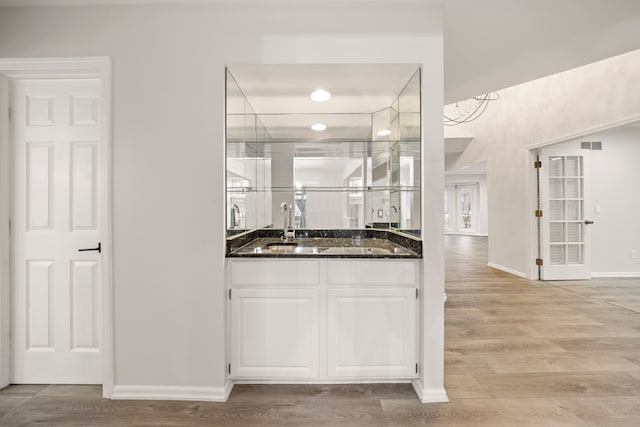 bar featuring light wood finished floors, baseboards, visible vents, and a sink