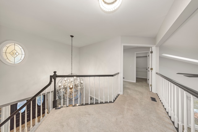 hall with an upstairs landing, carpet flooring, visible vents, and an inviting chandelier