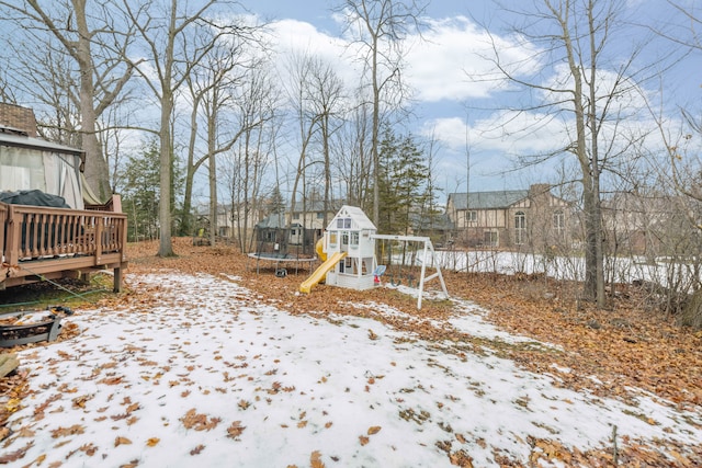 snowy yard featuring a trampoline, a playground, and a wooden deck