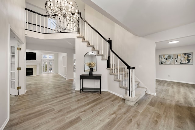 foyer entrance with stairs, a tiled fireplace, wood finished floors, and baseboards