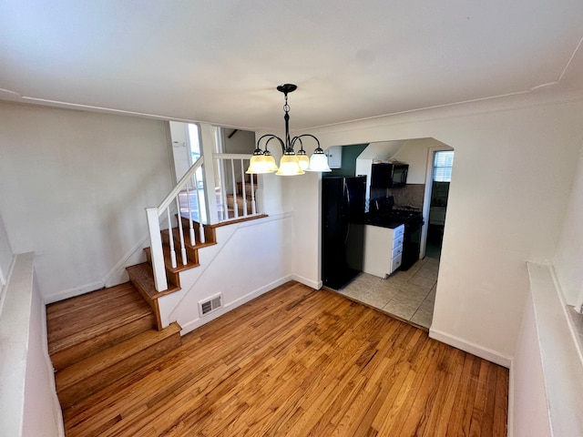 unfurnished dining area featuring visible vents, light wood-style flooring, stairway, an inviting chandelier, and baseboards