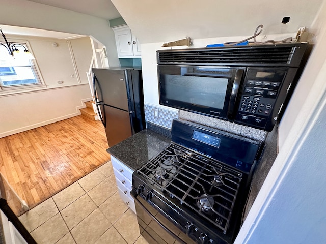 kitchen featuring light tile patterned floors, arched walkways, dark stone counters, white cabinets, and black appliances