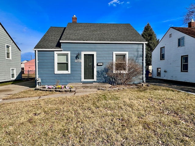 view of front of house with a shingled roof, a chimney, and a front lawn