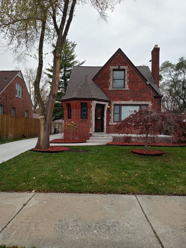 view of front of house with brick siding, a chimney, a front yard, and fence