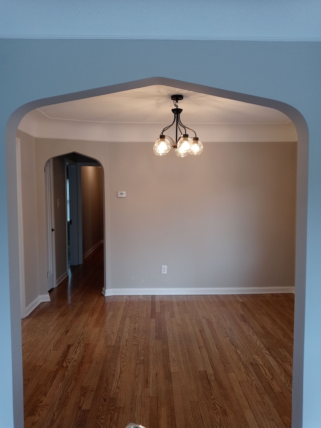 spare room featuring baseboards, arched walkways, a chandelier, and wood finished floors