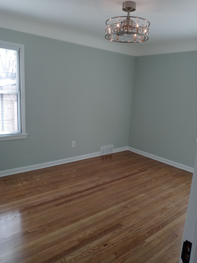 spare room with baseboards, visible vents, a chandelier, and dark wood-type flooring