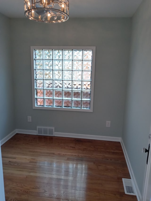 empty room featuring a notable chandelier, wood finished floors, visible vents, and baseboards