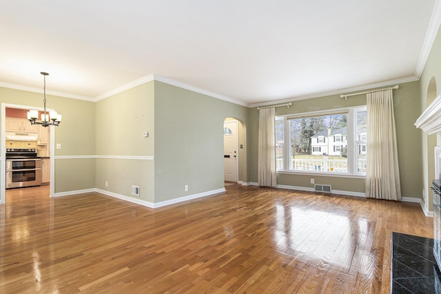 unfurnished living room with arched walkways, light wood finished floors, visible vents, a chandelier, and baseboards