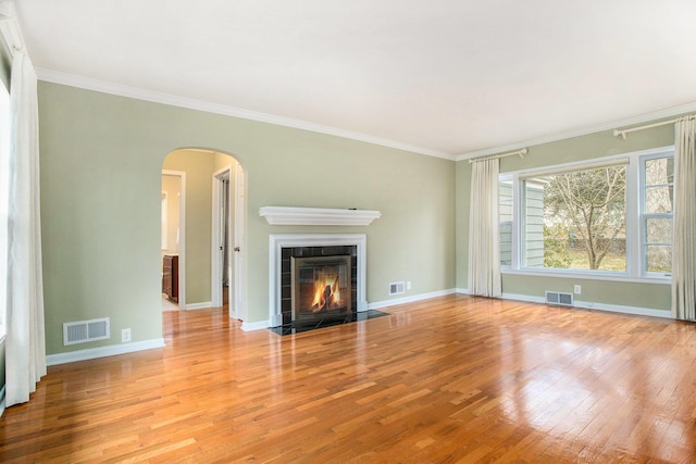 unfurnished living room with a tile fireplace, visible vents, arched walkways, and wood finished floors