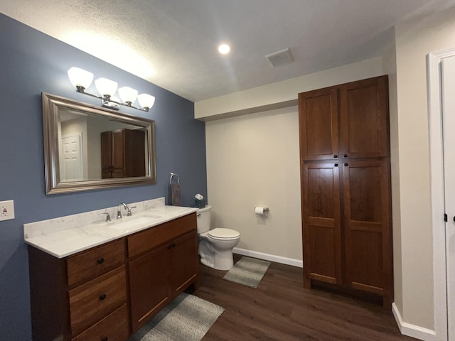 bathroom featuring toilet, wood finished floors, visible vents, vanity, and baseboards