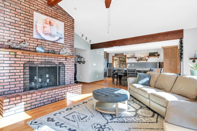 living room with beam ceiling, visible vents, a brick fireplace, wood finished floors, and baseboards