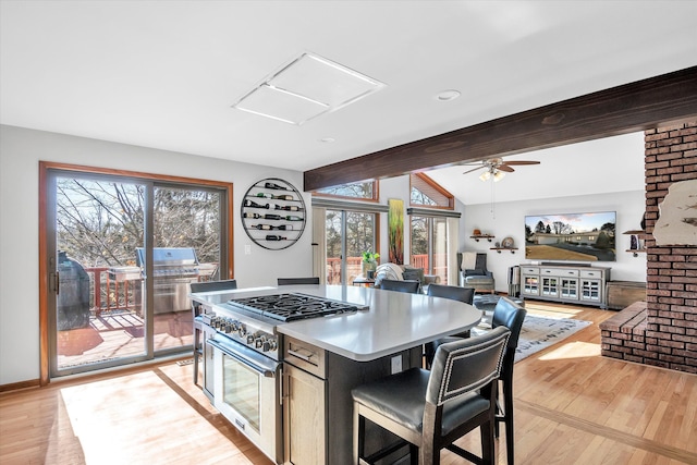 kitchen with lofted ceiling with beams, light wood finished floors, a kitchen island, and stainless steel stove