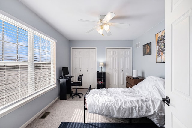 carpeted bedroom featuring a ceiling fan, visible vents, baseboards, and two closets