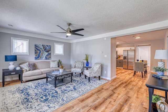 living area with a ceiling fan, baseboards, a textured ceiling, and light wood finished floors