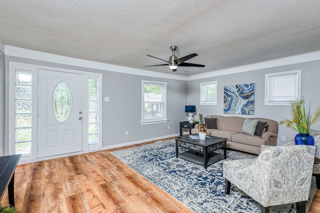 living room featuring a ceiling fan, a textured ceiling, baseboards, and wood finished floors