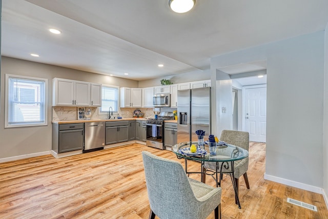 kitchen with light wood finished floors, baseboards, visible vents, stainless steel appliances, and gray cabinetry