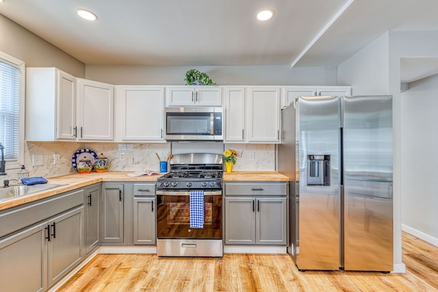 kitchen featuring appliances with stainless steel finishes, butcher block countertops, a sink, and gray cabinetry