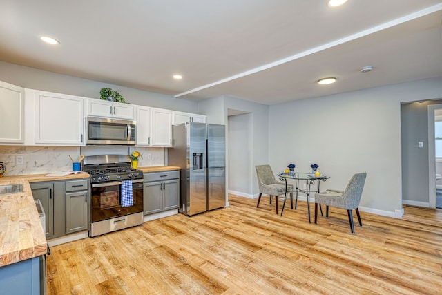 kitchen with stainless steel appliances, wood counters, white cabinets, light wood-style floors, and backsplash