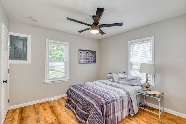 bedroom with light wood-style floors, electric panel, ceiling fan, and baseboards