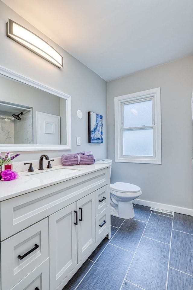 full bathroom with toilet, baseboards, tiled shower, and vanity