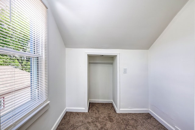 unfurnished bedroom with vaulted ceiling, dark colored carpet, and baseboards