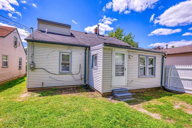 rear view of property featuring entry steps, a lawn, and fence