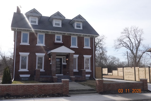 view of front facade featuring brick siding, roof with shingles, and fence