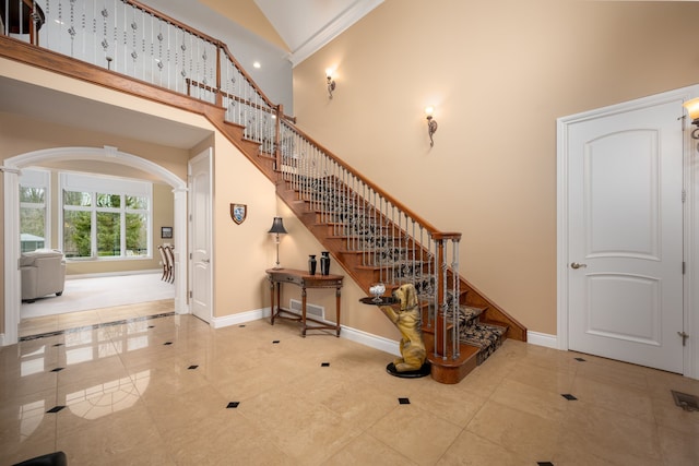 staircase featuring baseboards, high vaulted ceiling, and arched walkways