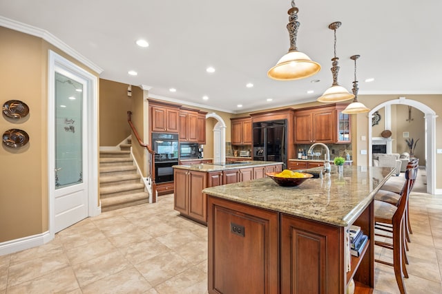 kitchen featuring arched walkways, a large island, brown cabinetry, a sink, and black appliances