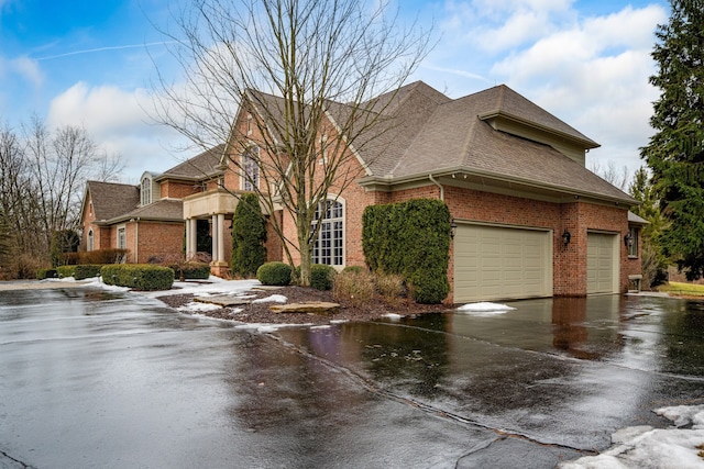 view of front of house with driveway, brick siding, roof with shingles, and an attached garage